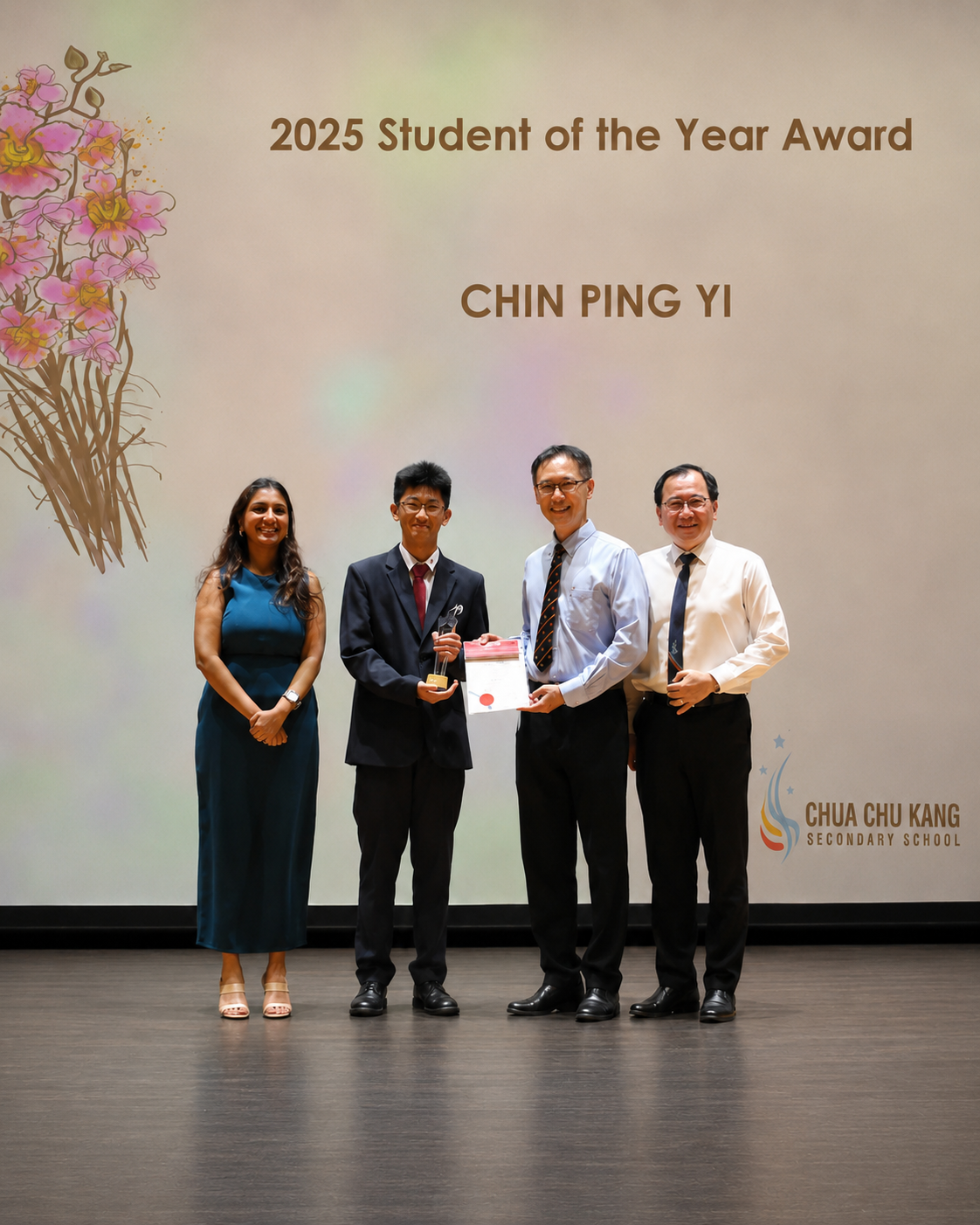 One student in a blazer holds a trophy and certificate while posing with three adults on stage.